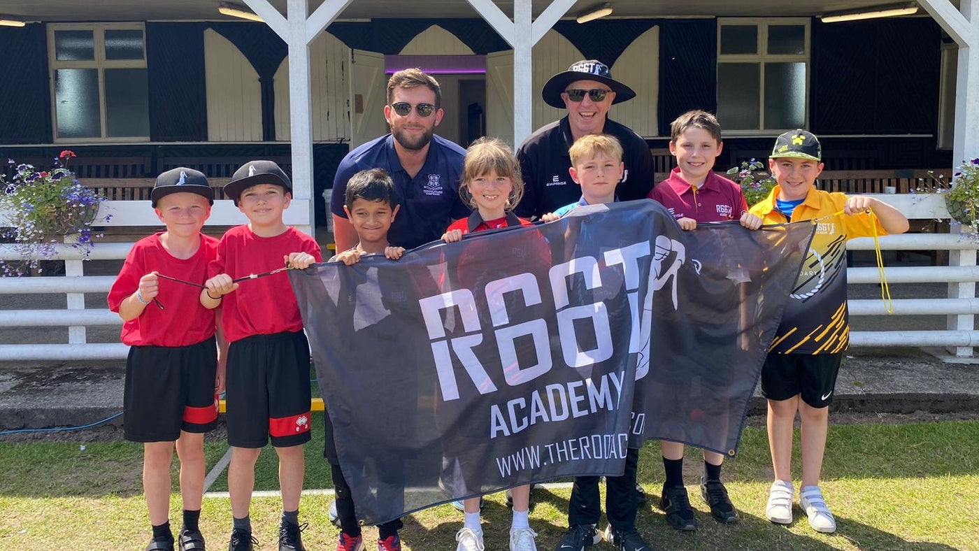 Group of children and two adults holding a 'Root Academy' banner in front of a building.