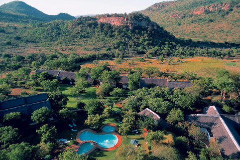 Aerial view of a resort with a pool surrounded by lush greenery and mountains.