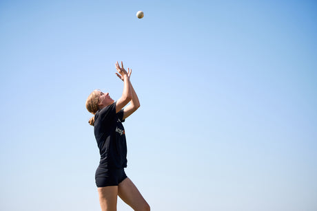 Person in a black sports outfit catching a ball against a clear blue sky