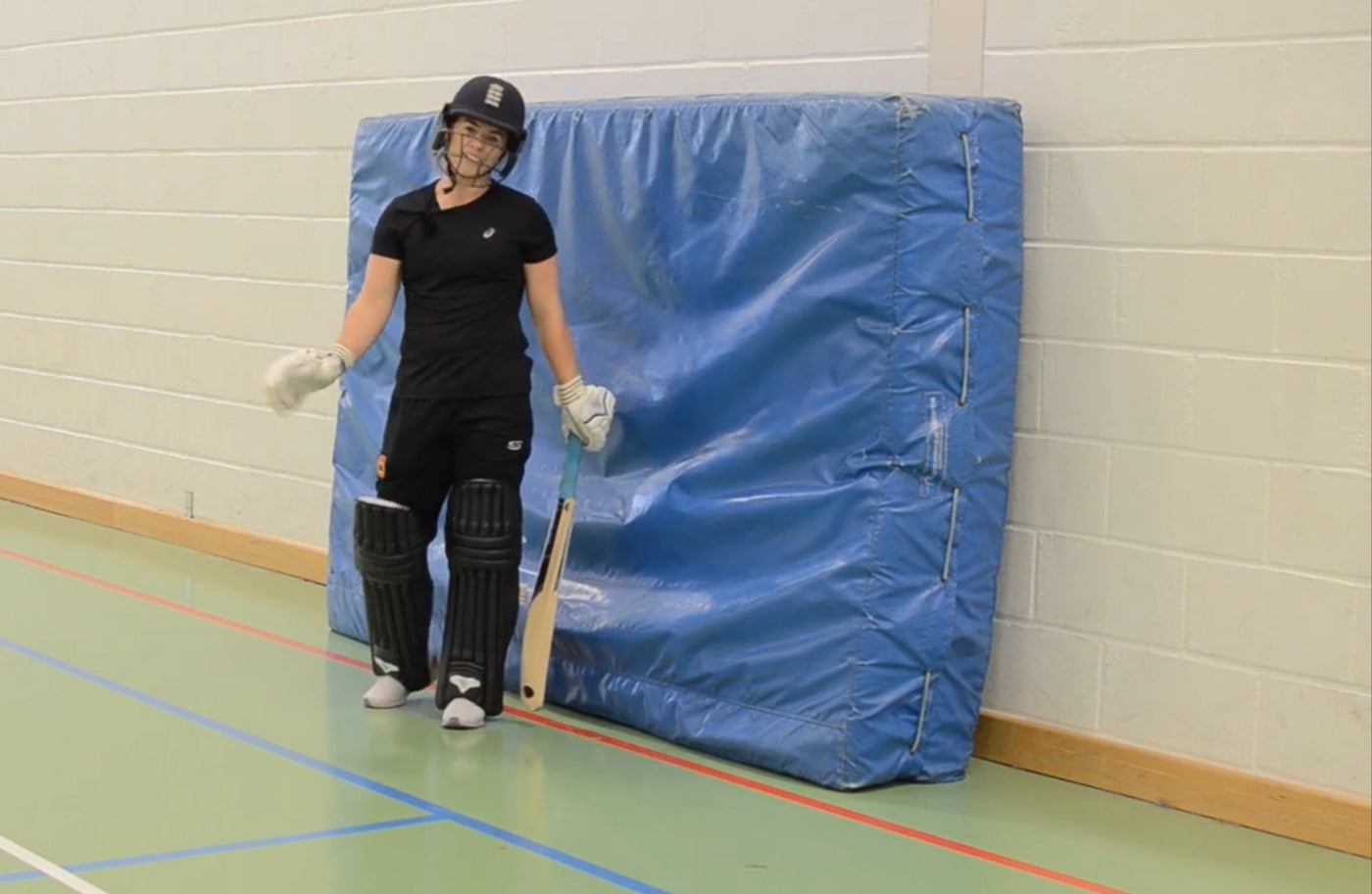 Woman in cricket gear standing infront of a blue mat
