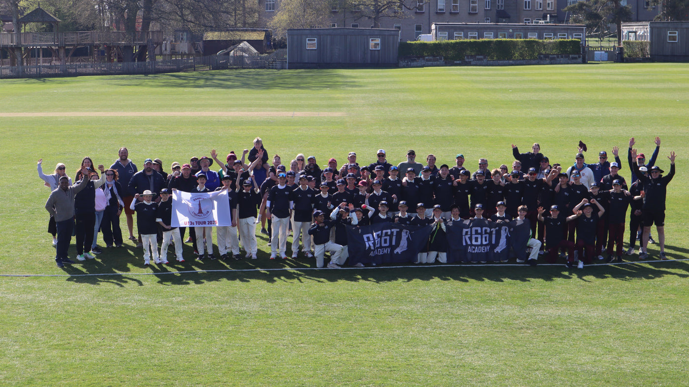 Large group of people on a cricket field with 'R66T Academy' banners