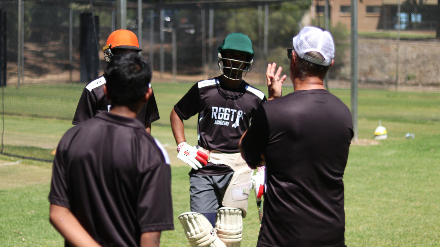 Three cricket players in discussion with their coach