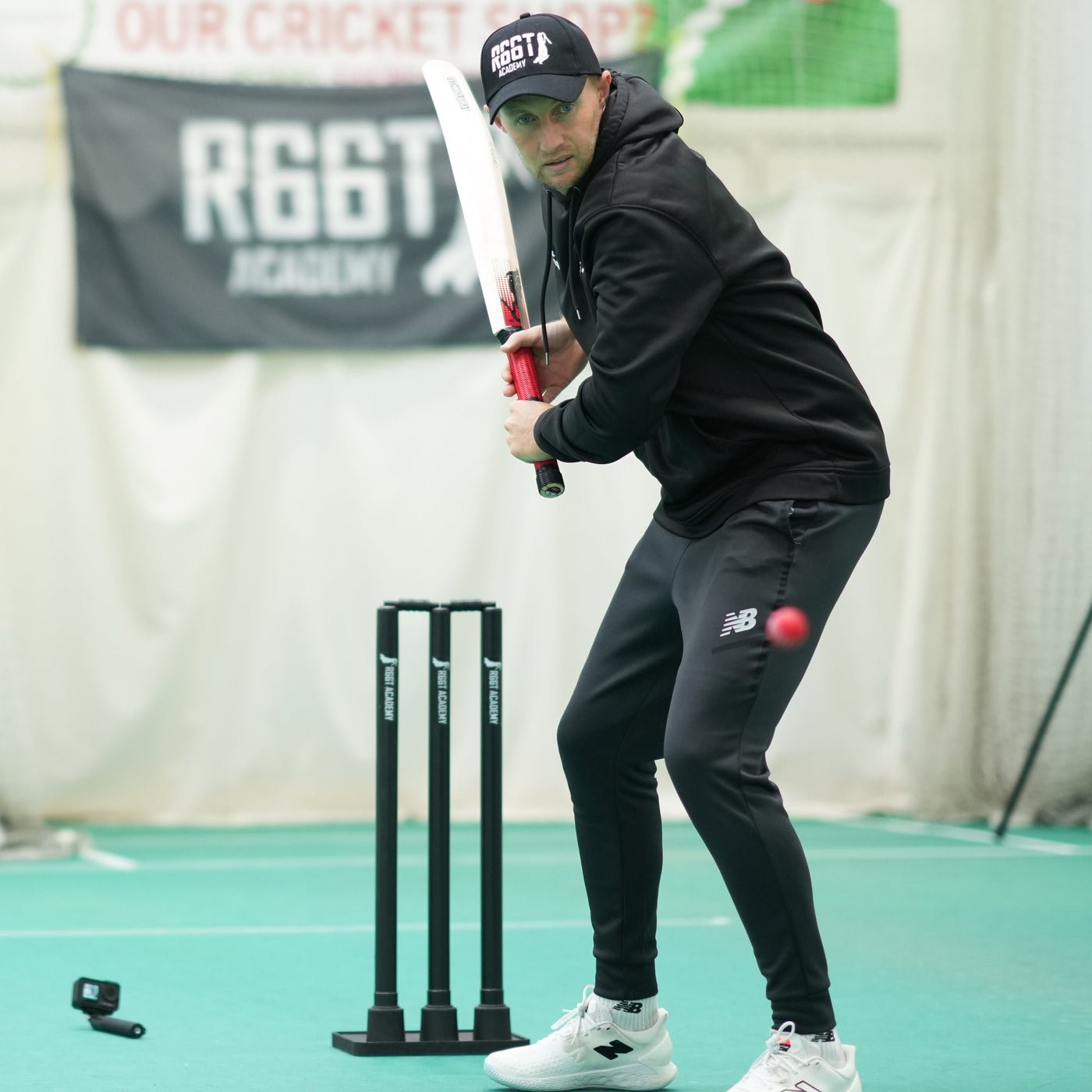 Joe Root practicing cricket batting in a indoor setting with 'R66T' branding.