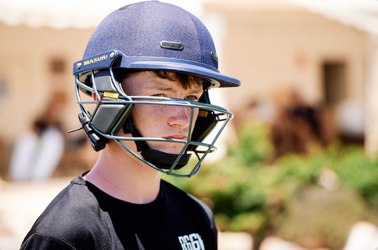 Person wearing a blue cricket helmet with a faceguard outdoors