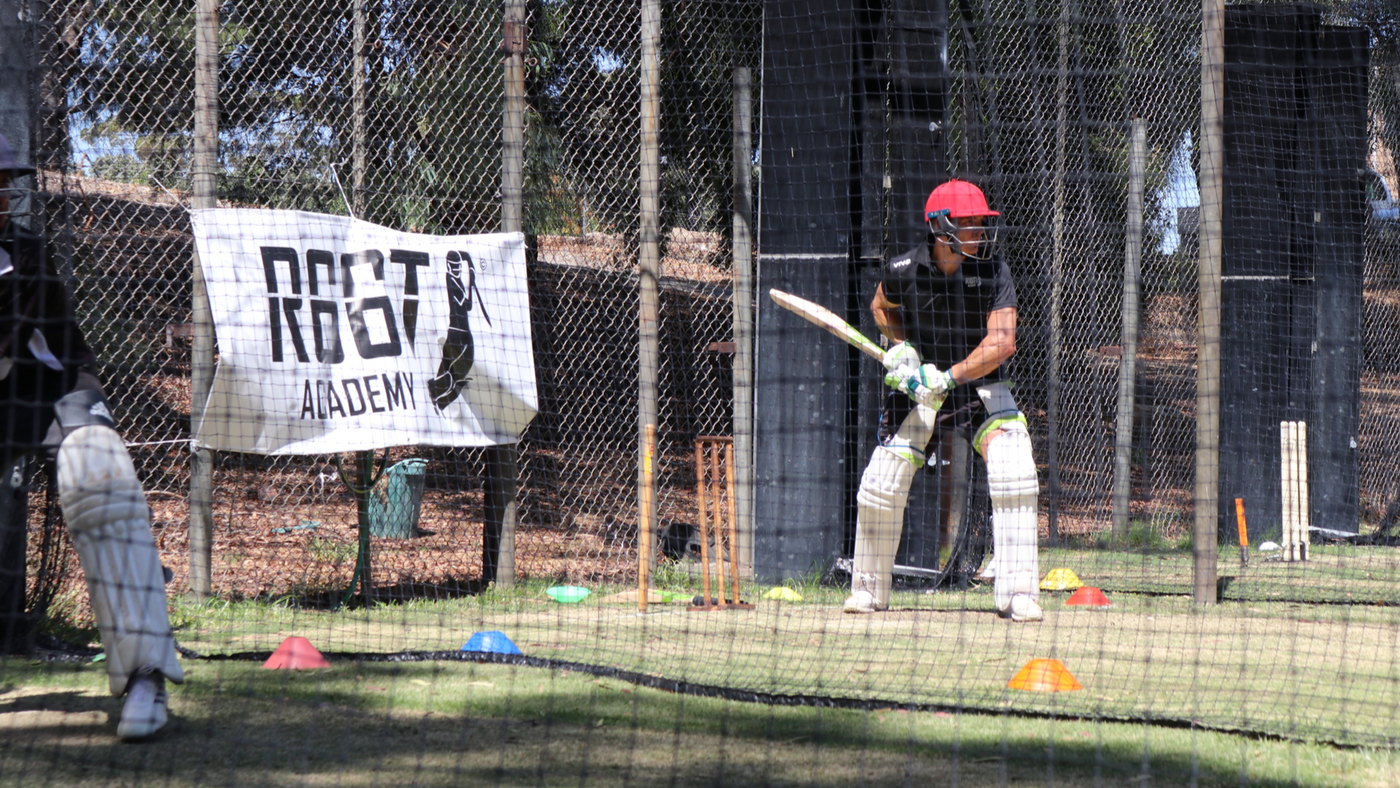 Person playing cricket in a net session with a banner in the background