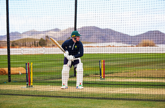 Person playing cricket in a net session with mountains in the background
