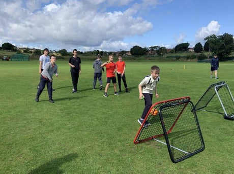Children outdoors on grass practicing crickets with small nets