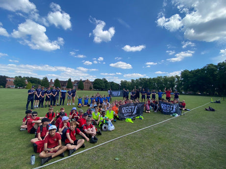 Groups of cricket teams sat outdoors on a grassy field with three 'R66T Academy' logos