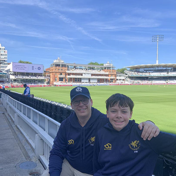 Two people in matching navy blue hoodies with a logo on at Lord's Cricket Ground.
