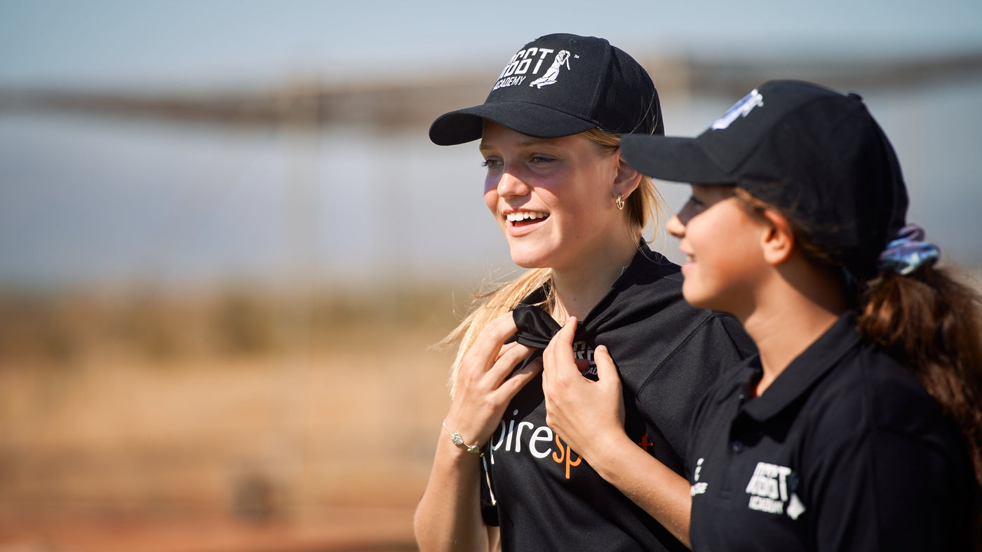 Two people wearing black caps and shirts with logos, standing outdoors.