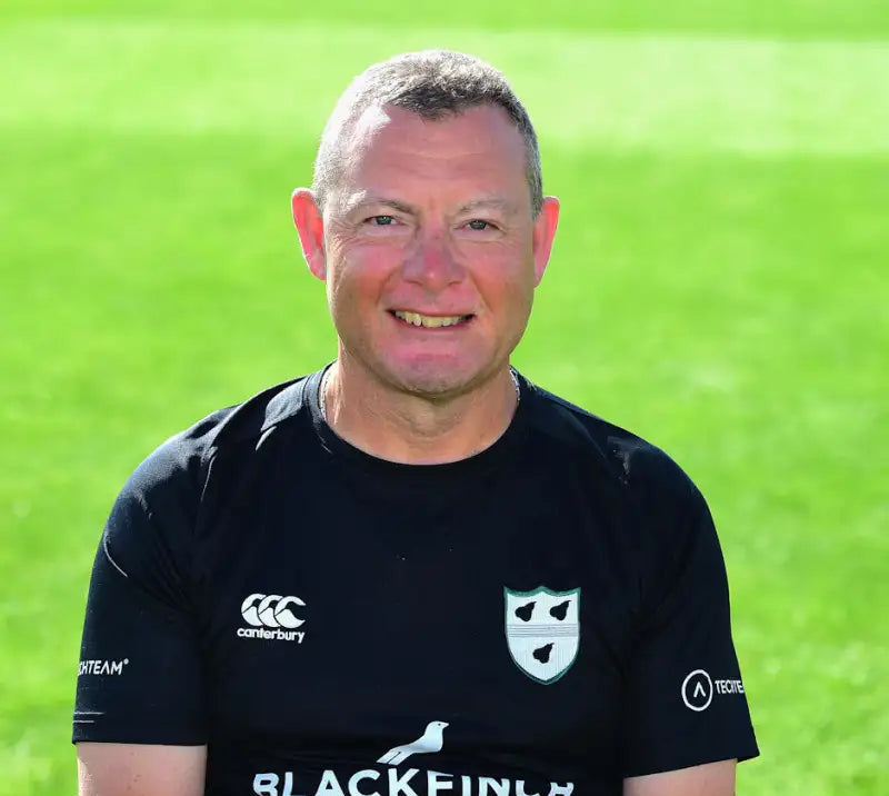 Man wearing a black sports jersey with logos on a green field background