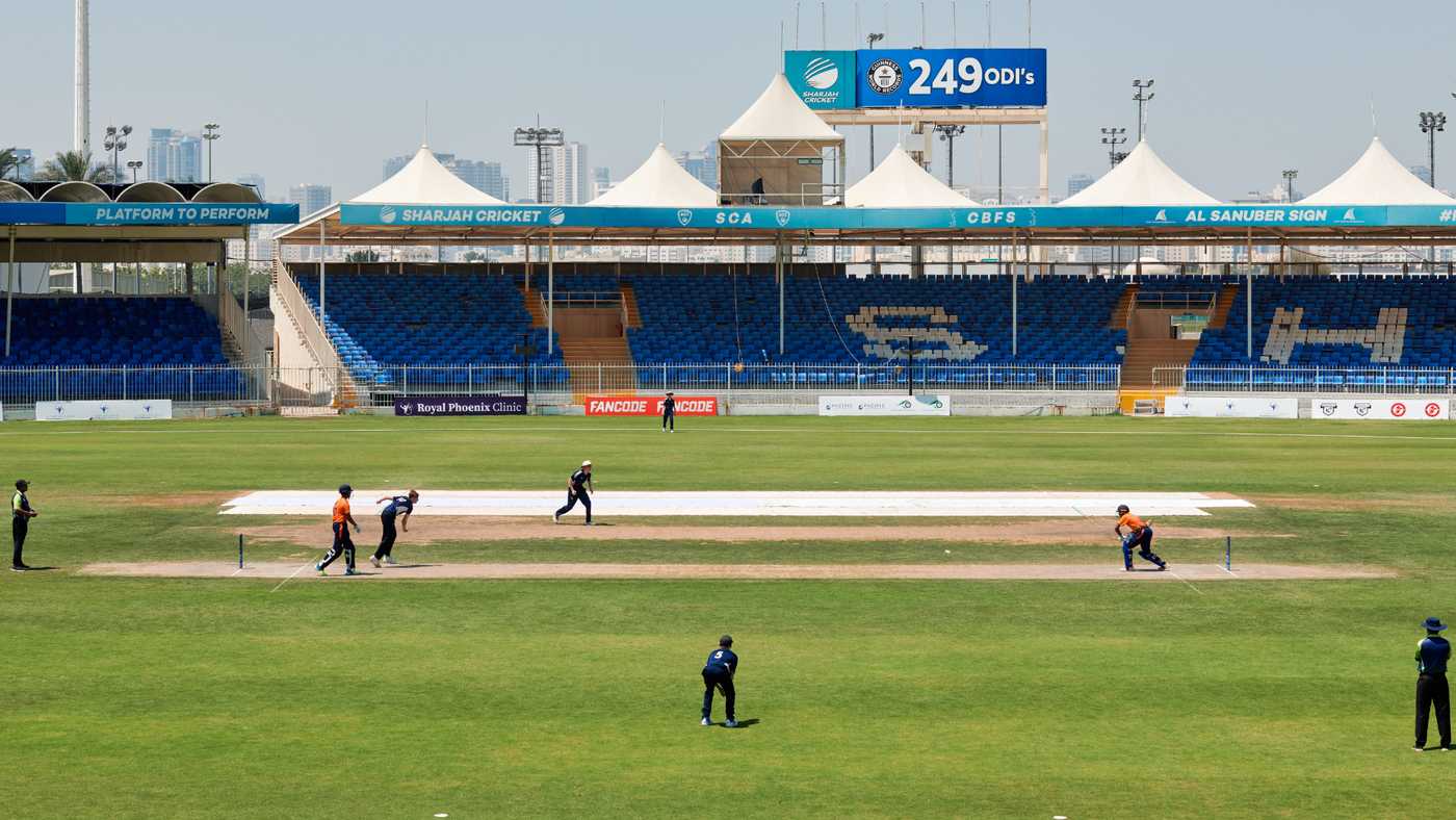 Cricket match in progress in Dubai on a green field with stadium seating and advertisements in the background.