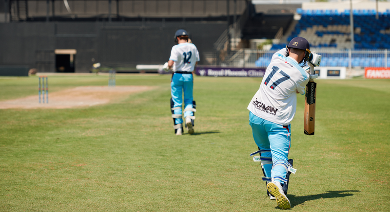 Two cricketers in action on a cricket field with stadium in the background in Dubai