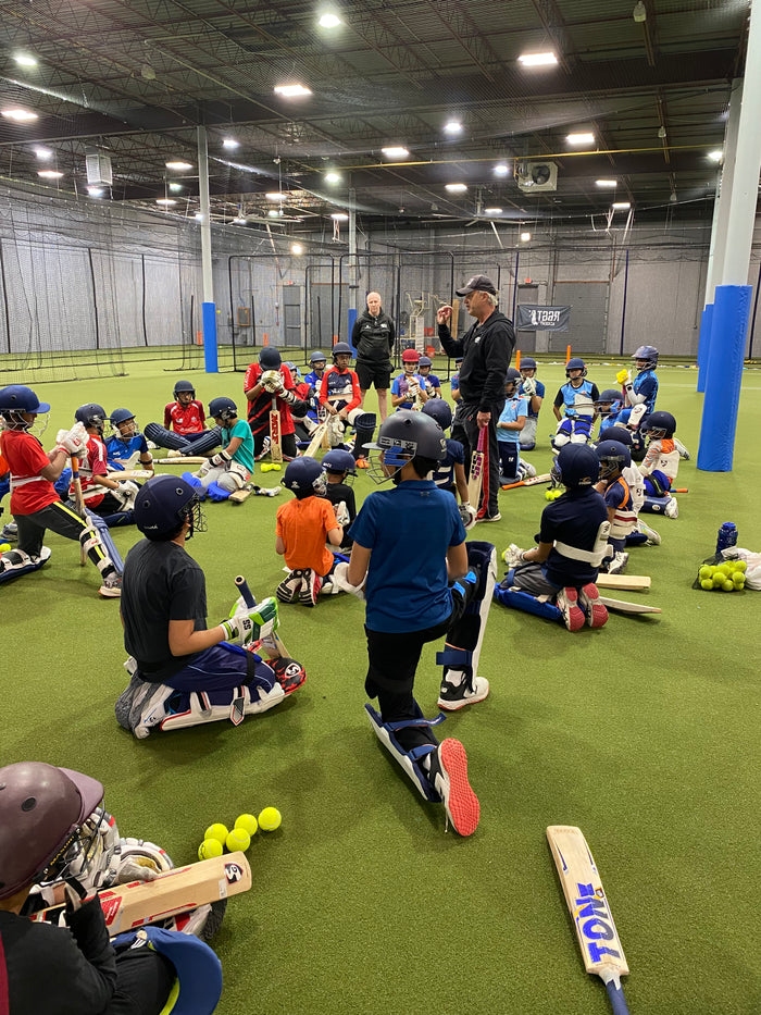 Children participating in a cricket training session indoors with coaches and equipment.