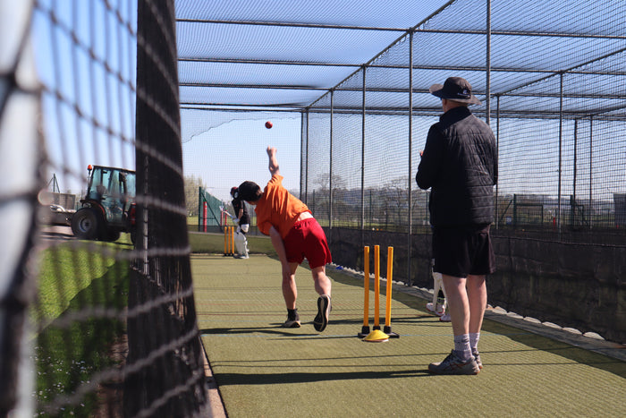 Two people playing cricket in an outdoor net on one side.
