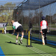 People playing cricket in a netting area with stumps and bails.