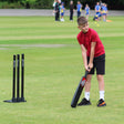 Child playing cricket on a grass field with R66T Academy cricket bats and stumps.