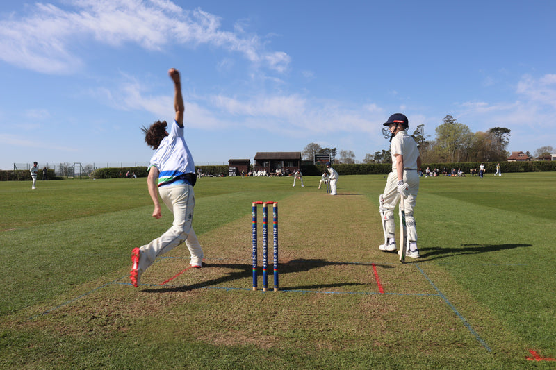 Cricketer bowling during a match on a grass field with a clear sky.