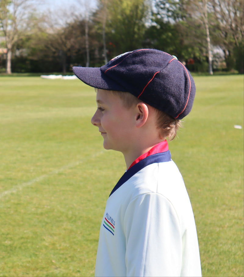 Young boy wearing a navy cap and white shirt with red and blue accents on a grassy field.