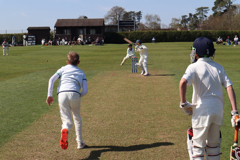 Cricketers in action on a cricket field with a clear sky