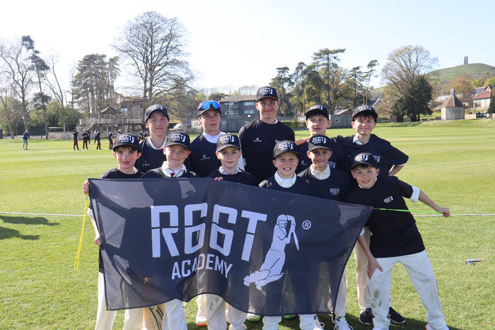 Group of young cricket players holding a banner with 'R66T Academy' on a grassy field.