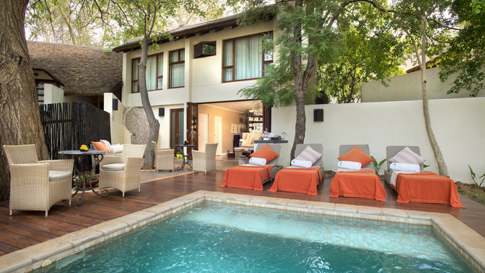 Outdoor seating area with orange cushions by a poolside in a residential setting