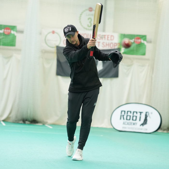 Person practicing batting in an indoor sports facility with 'R66T Academy' branding.