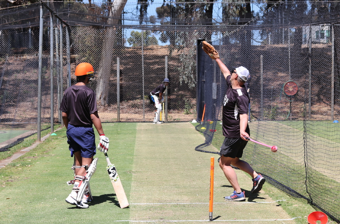Two people playing cricket in a netted area with sports equipment.