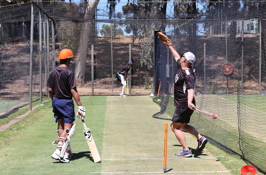 Two people playing cricket in a netted area with sports equipment.
