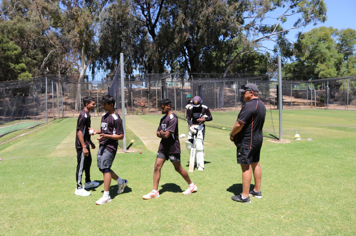 Group of cricket players practicing on a field with trees in the background