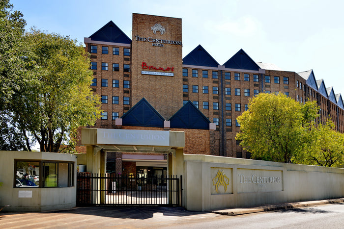 Brick building with 'The Centurion' sign, surrounded by trees on a sunny day.